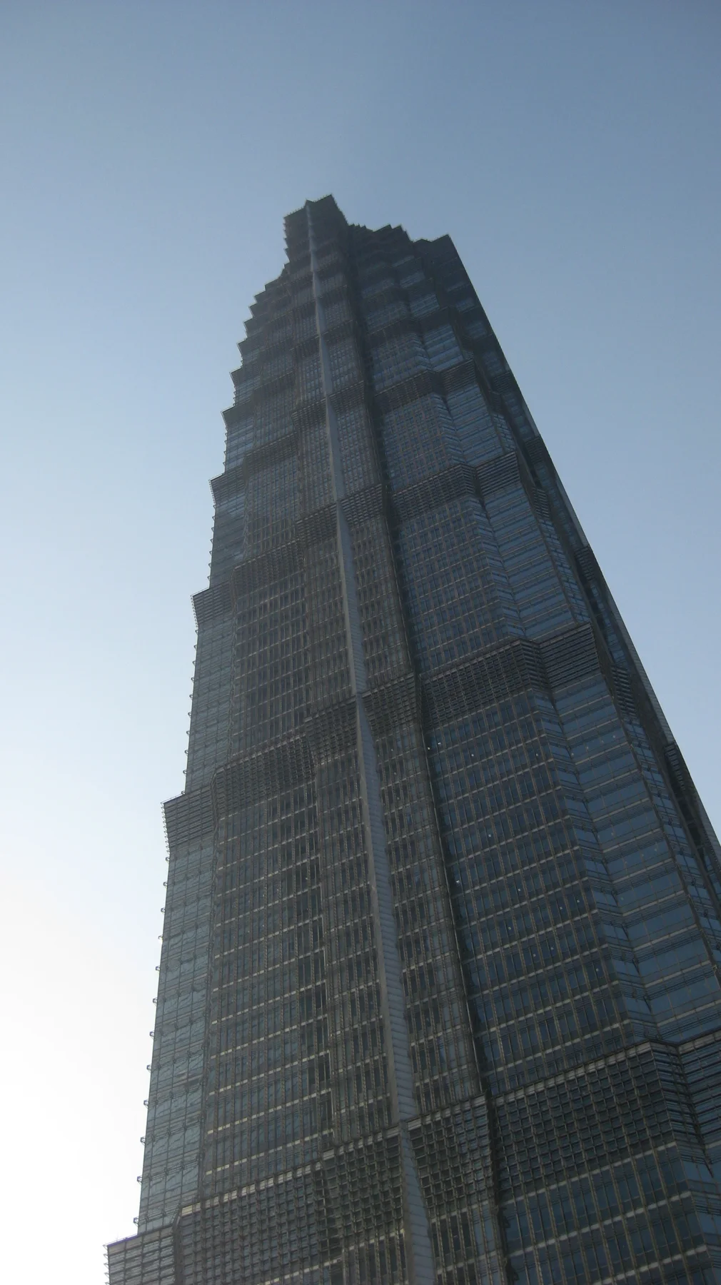 A tall tiered skyscraper narrows towards its pointed top in an upward view from street level.