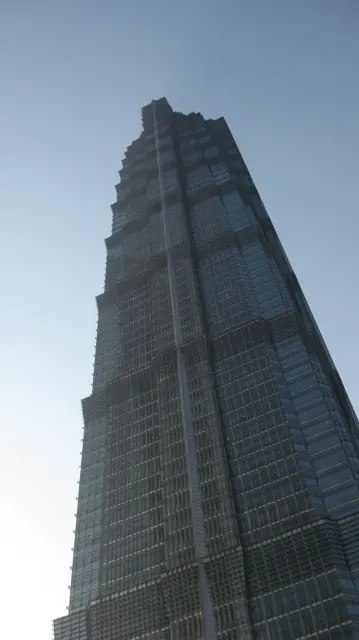 A tall tiered skyscraper narrows towards its pointed top in an upward view from street level.
