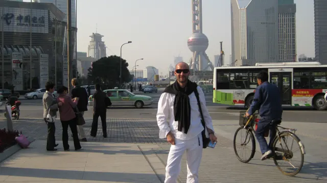 A person in white stands near a street crossing with buses, cyclists and tall buildings behind.