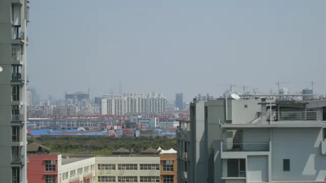 Buildings and a broad construction area extend into the distance beyond nearby balconies and rooftops.