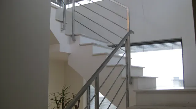 Pale stairs turn around a metal railing inside a bright white-walled interior.