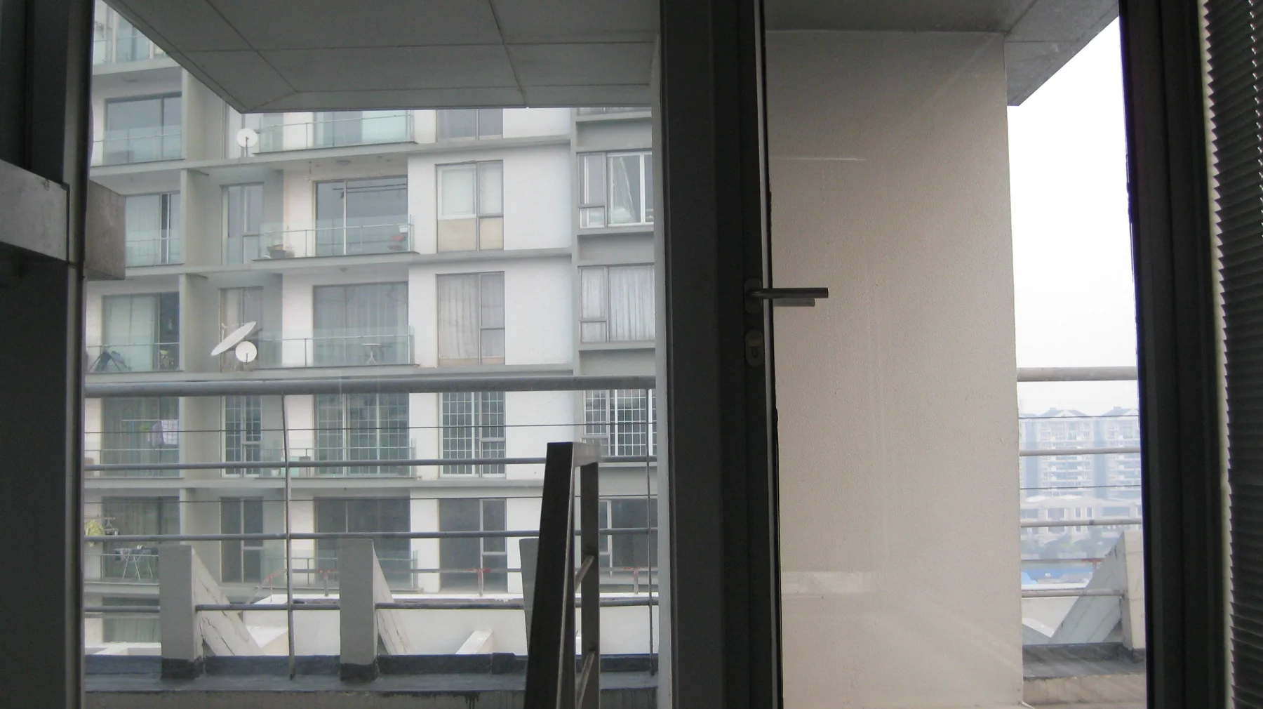 A view through a glass door looks towards stacked balconies on a neighbouring apartment building.
