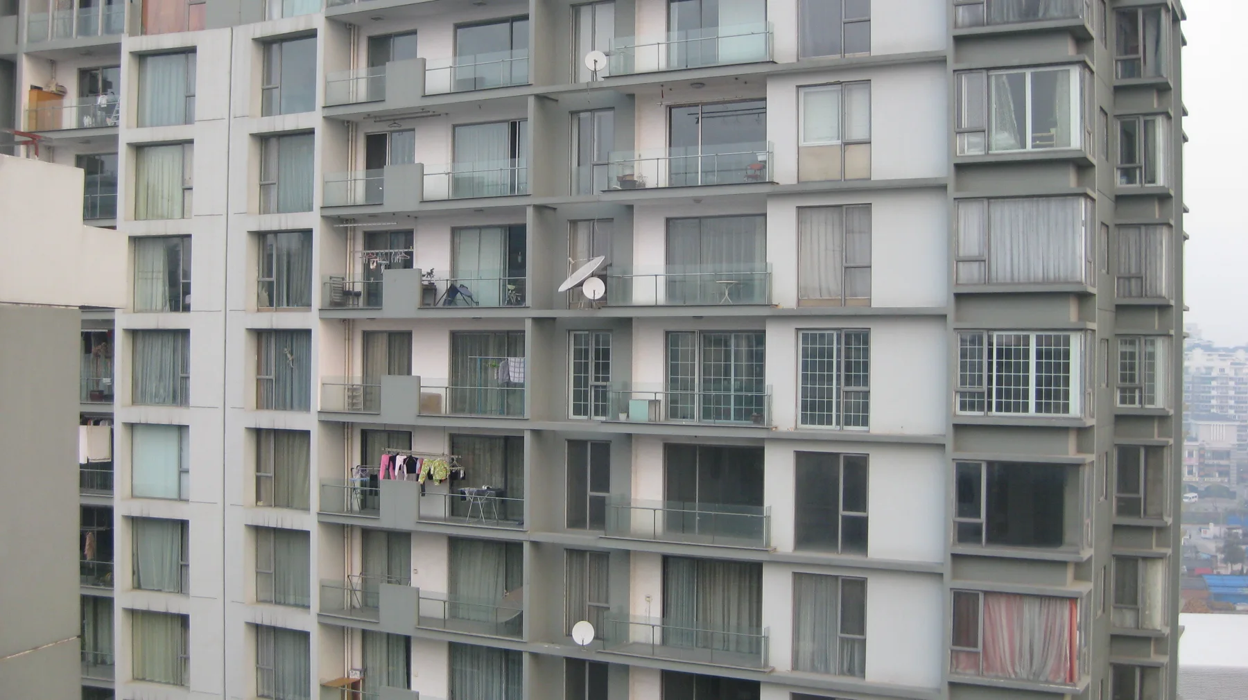 Rows of windows, balconies and satellite dishes cover the facade of an apartment building.