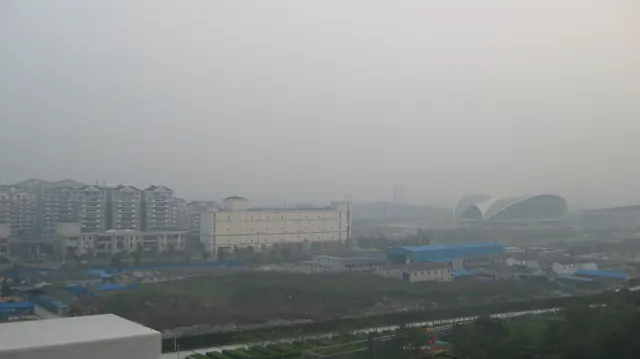 Low buildings, open ground and distant structures fade into a pale hazy skyline.