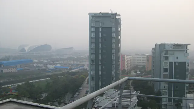 A tall residential building rises beyond a balcony railing, with roads and lower buildings below.