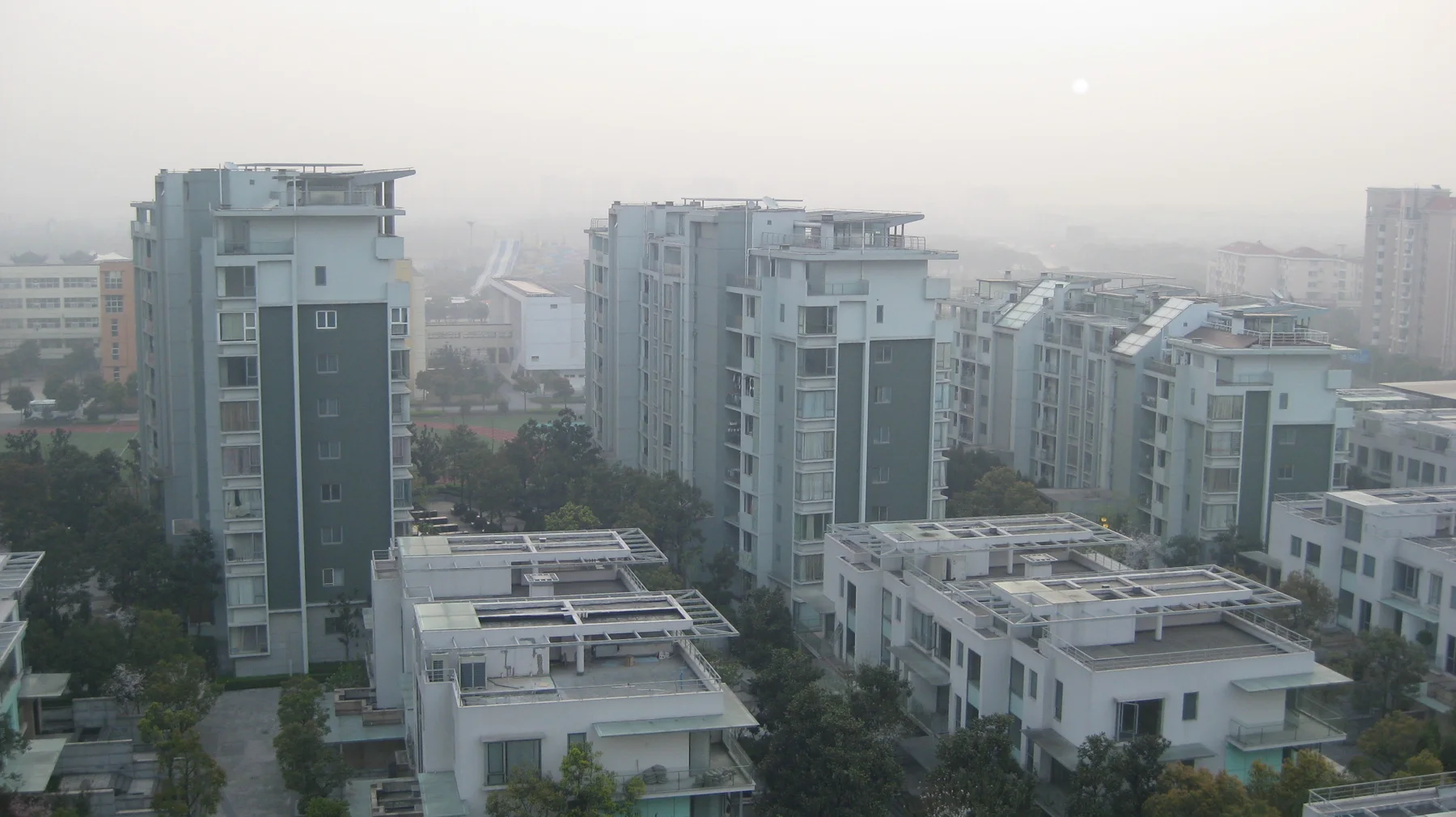 Modern apartment blocks and lower flat-roofed homes fill an elevated view through soft haze.