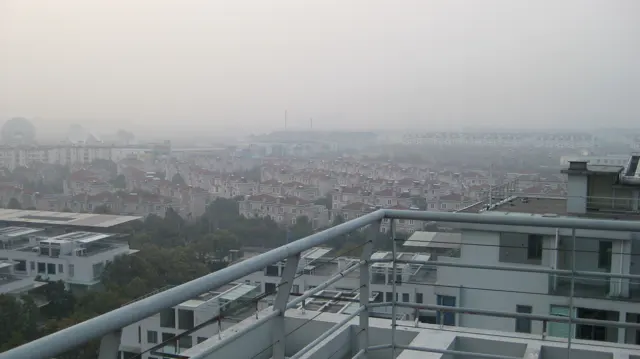 A balcony railing crosses an elevated view of closely packed rooftops fading into the haze.