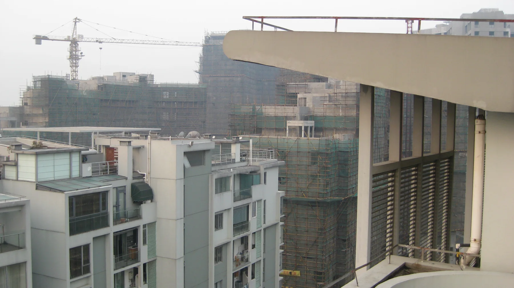 A construction crane rises beyond nearby apartment buildings and a projecting balcony roof.