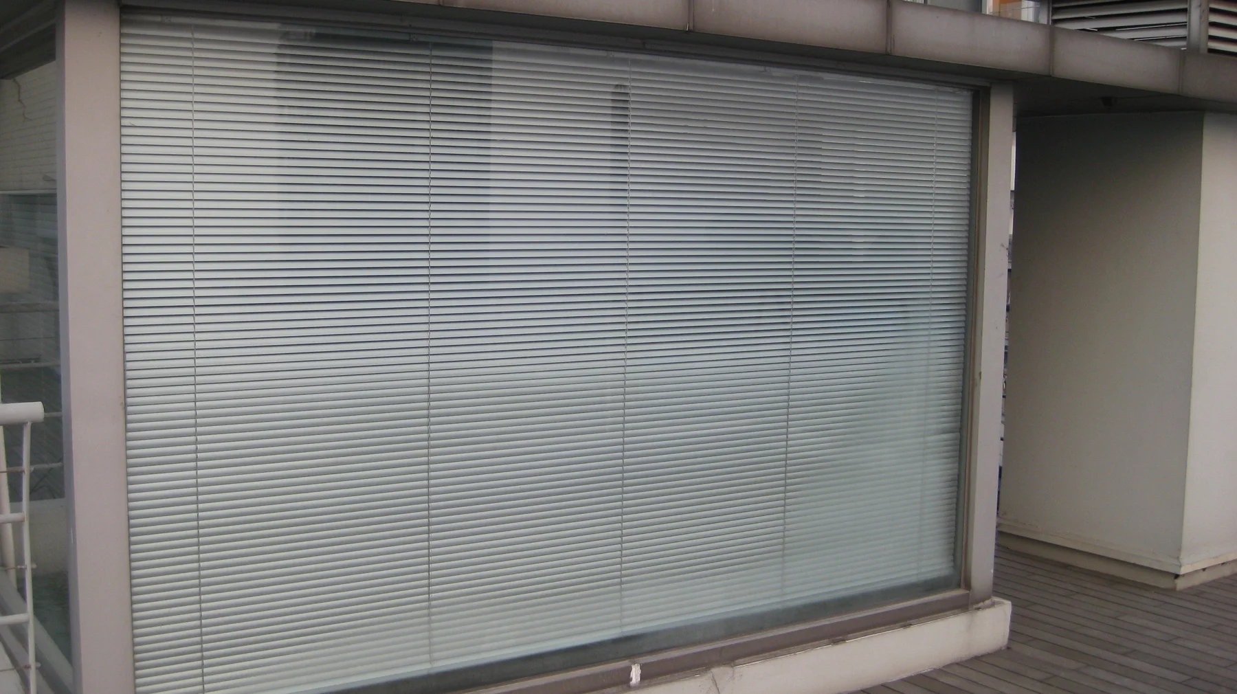 Closed horizontal blinds cover a broad glazed opening beside a narrow outdoor deck.