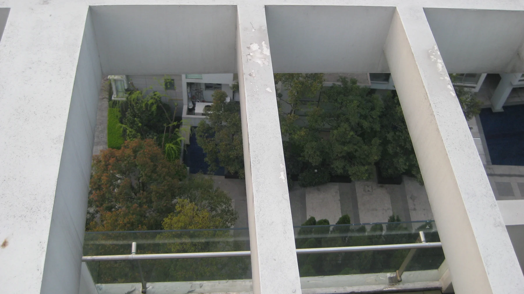 An overhead view through pale structural beams looks down towards a planted courtyard and balconies.
