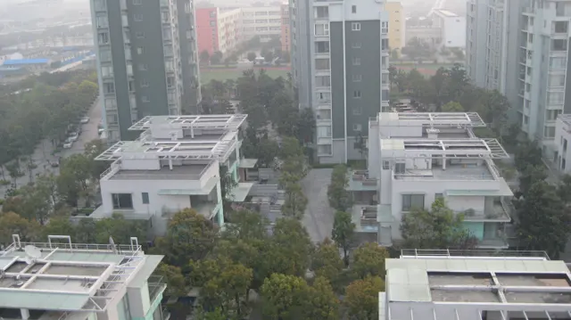 A straight landscaped path runs between white residences towards tall apartment blocks, seen from above.