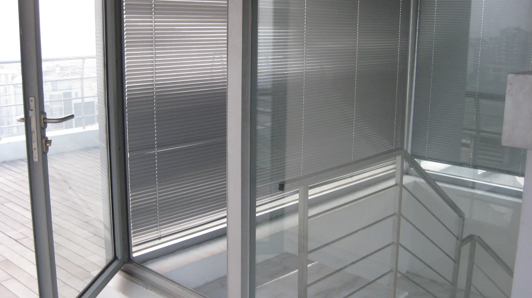 A stair landing with metal railings sits beside floor-to-ceiling glazing and horizontal blinds.