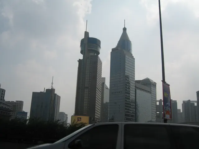 Several tall buildings rise beneath clouds, seen over the dark edge of a car window.