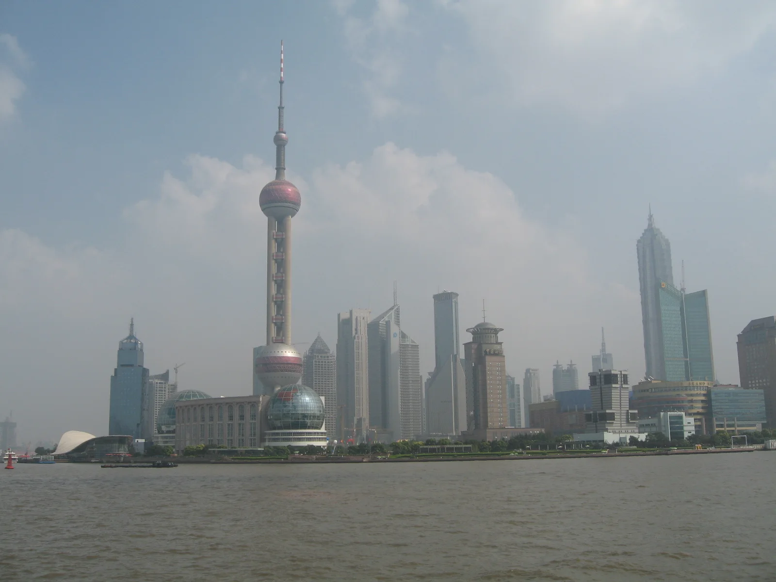 A tower with spherical sections rises among high-rises across a broad river under a pale blue sky.