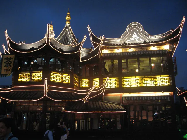 Ornate multi-storey facades with upturned roofs shine with golden light beneath a deep blue sky.