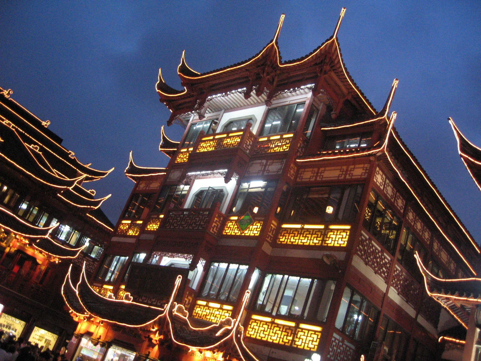An angled upward view follows a red multi-level building with bright windows and illuminated roof edges.