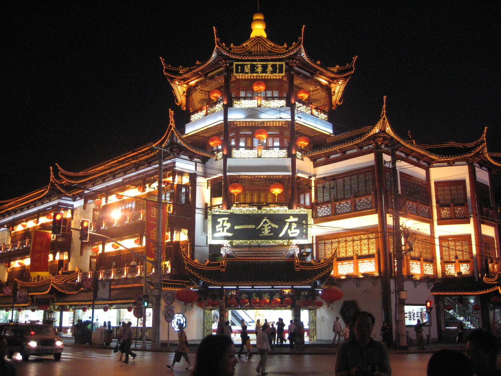 A tall ornate corner building glows with red and golden lighting above a busy pedestrian area.
