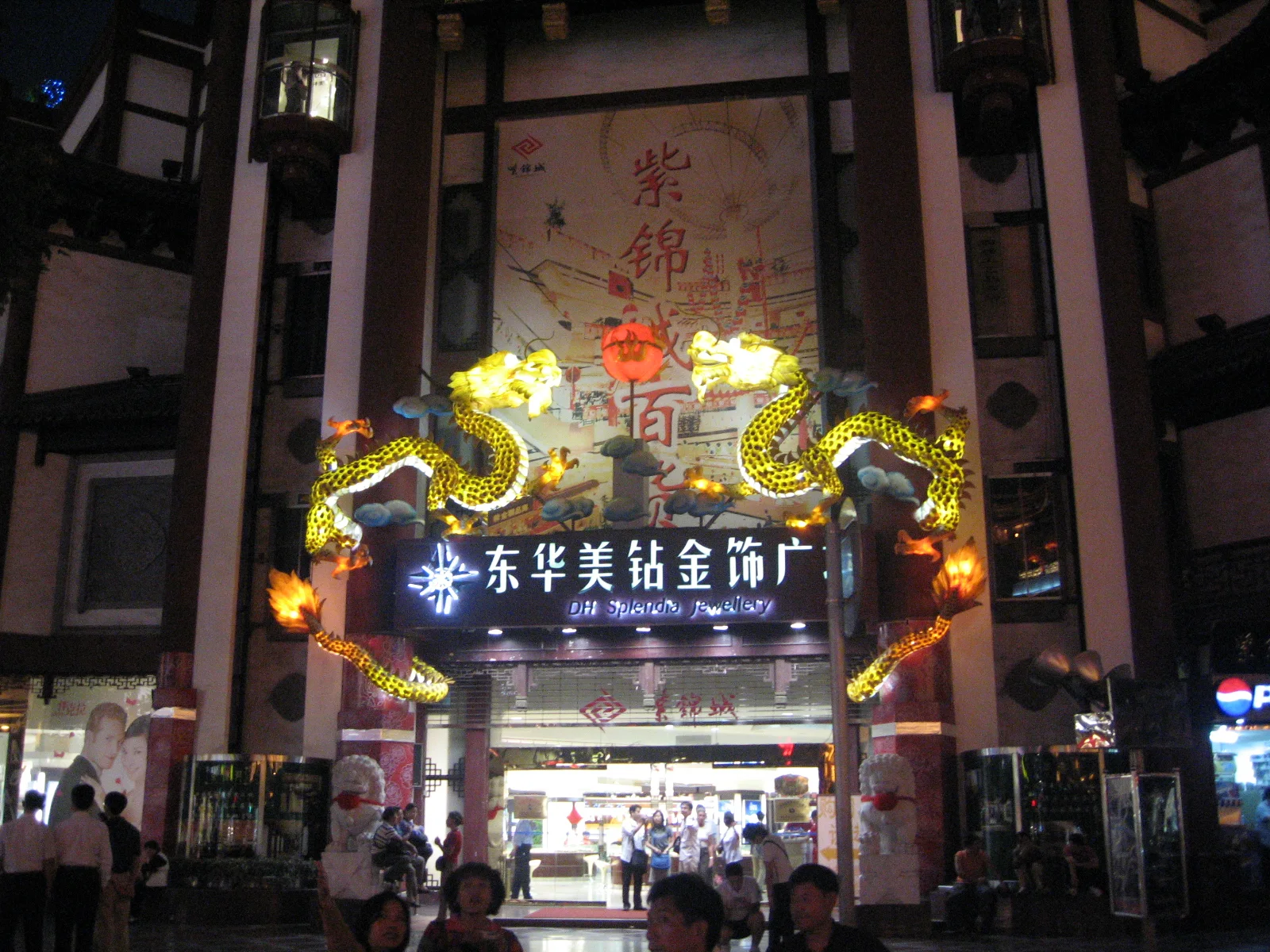 A large illuminated entrance with dragon-shaped decoration and Chinese lettering opens onto a crowded shopping area.