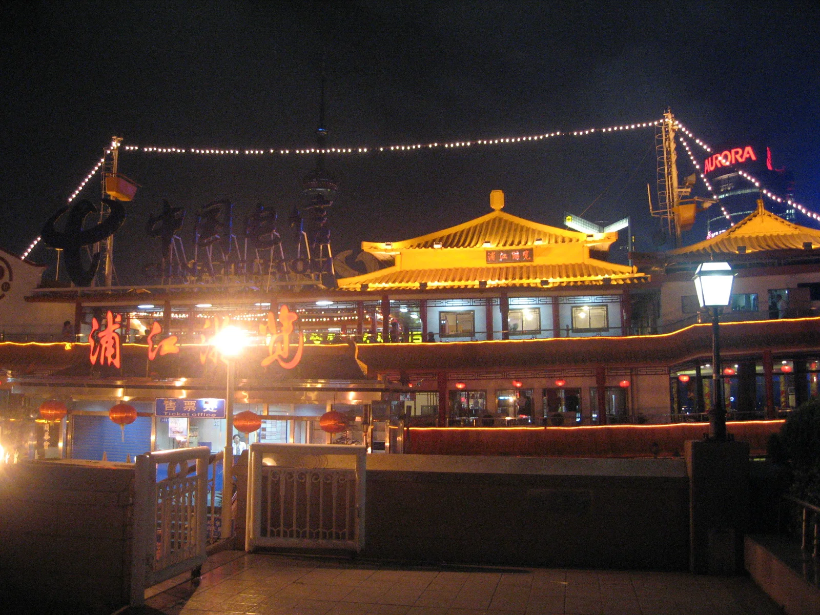 A boat with glowing yellow rooflines and strings of lights sits at the waterfront after dark.