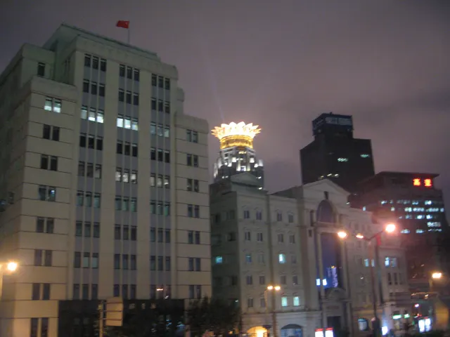 Lit windows and a brightly crowned tower rise above a city street beneath a purple-grey night sky.