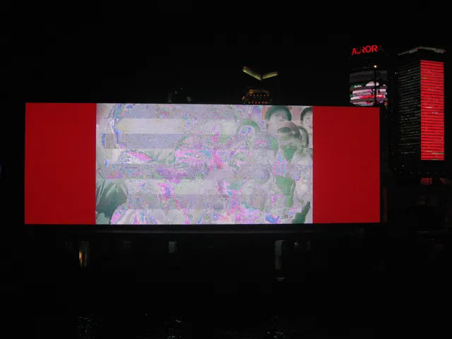 A large screen with red borders and a pale central image glows beside the river at night.
