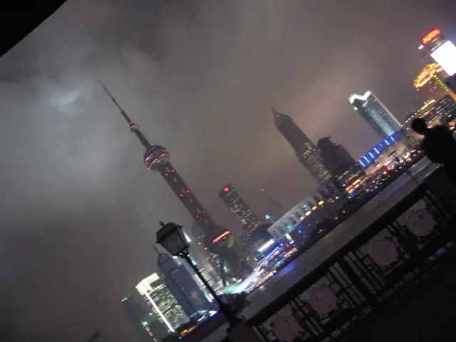 A tilted night view frames the tower and skyline above a dark decorative riverside railing.