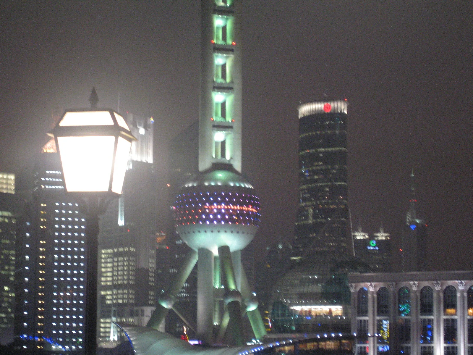 A bright street lamp stands in front of a green-lit spherical tower and nearby illuminated buildings.