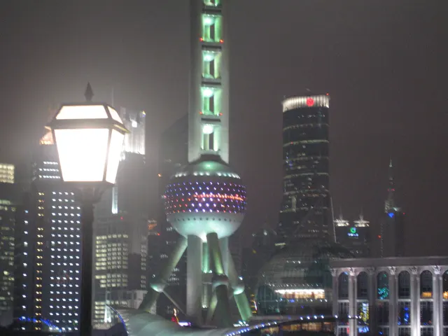 A bright street lamp stands in front of a green-lit spherical tower and nearby illuminated buildings.