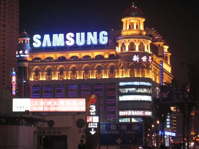 A large Samsung sign crowns a warmly lit building with an ornate corner tower above other illuminated signs.