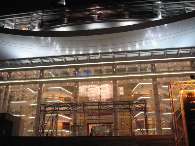 A large glazed facade reveals warm interior lighting beneath a broad curved overhanging roof at night.