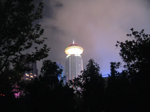 A tower with a glowing circular top rises behind silhouetted trees in a purple-grey night sky.