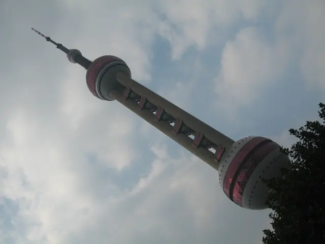 A tower with pink spherical sections stretches diagonally across a partly cloudy daytime sky.
