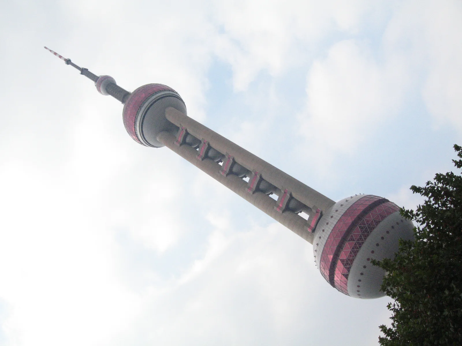 A low angled view follows a spherical-section tower across a bright cloud-filled sky.