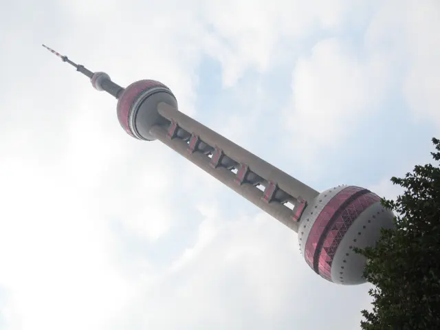 A low angled view follows a spherical-section tower across a bright cloud-filled sky.