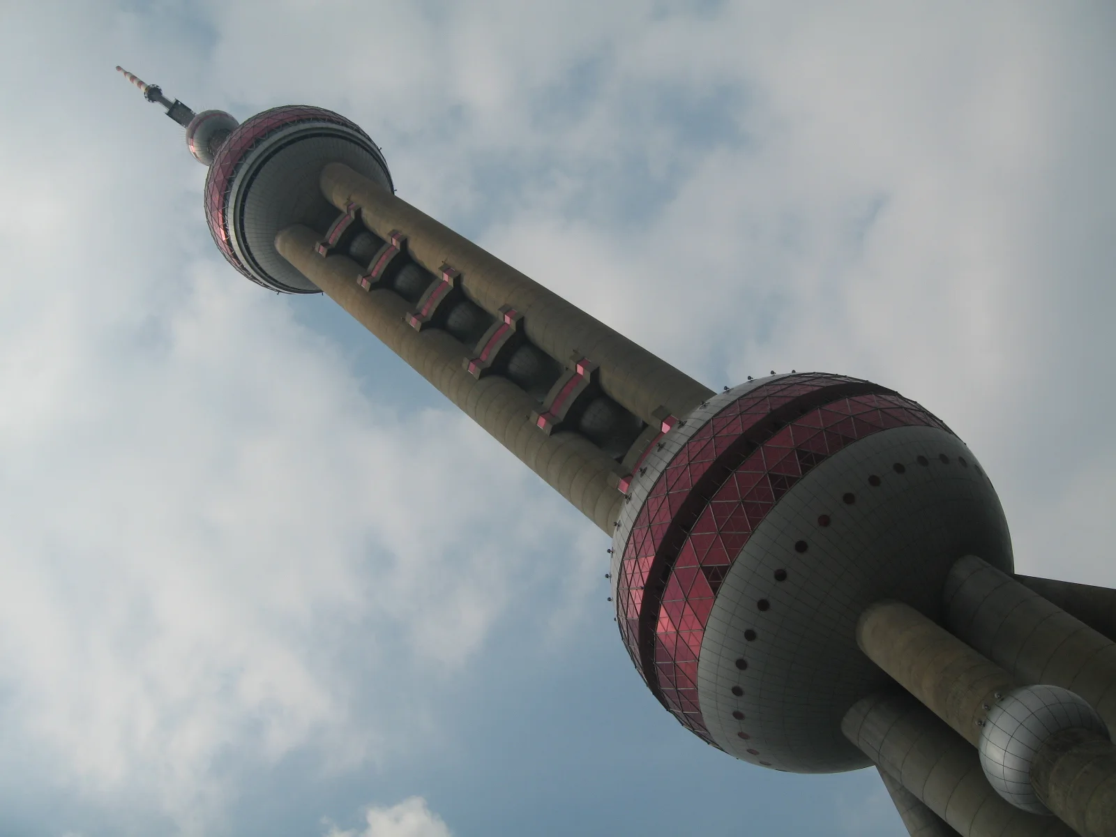 A low oblique view frames the tower and its pink bands against clouds, with dark leaves along one edge.