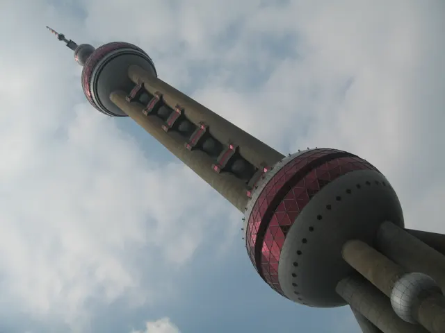 A low oblique view frames the tower and its pink bands against clouds, with dark leaves along one edge.