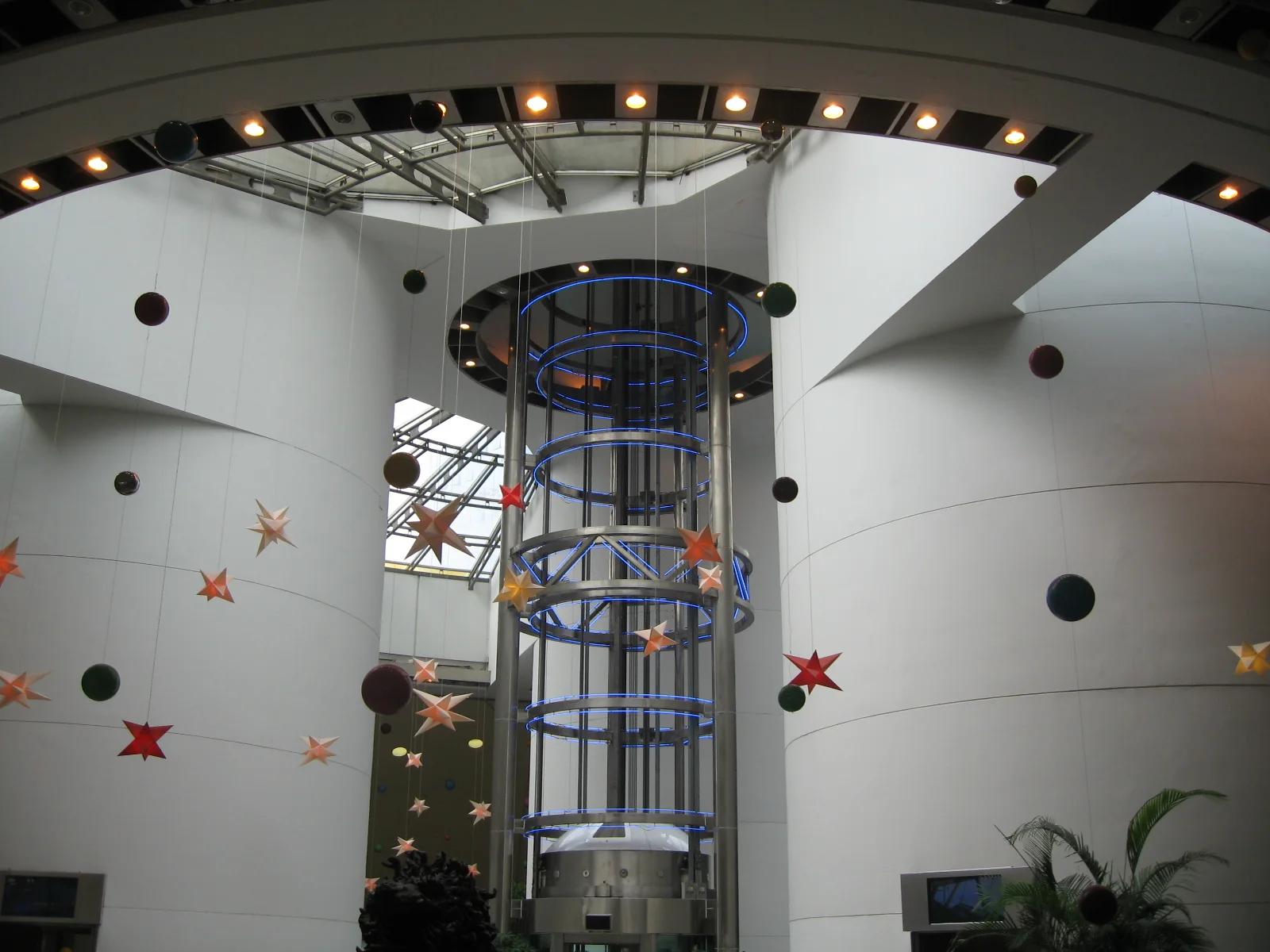 A cylindrical glass lift rises through a bright curved atrium decorated with stars and circular wall openings.