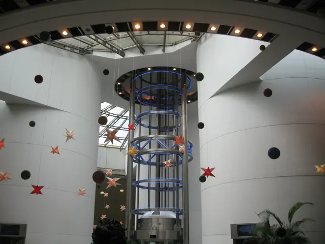 A cylindrical glass lift rises through a bright curved atrium decorated with stars and circular wall openings.