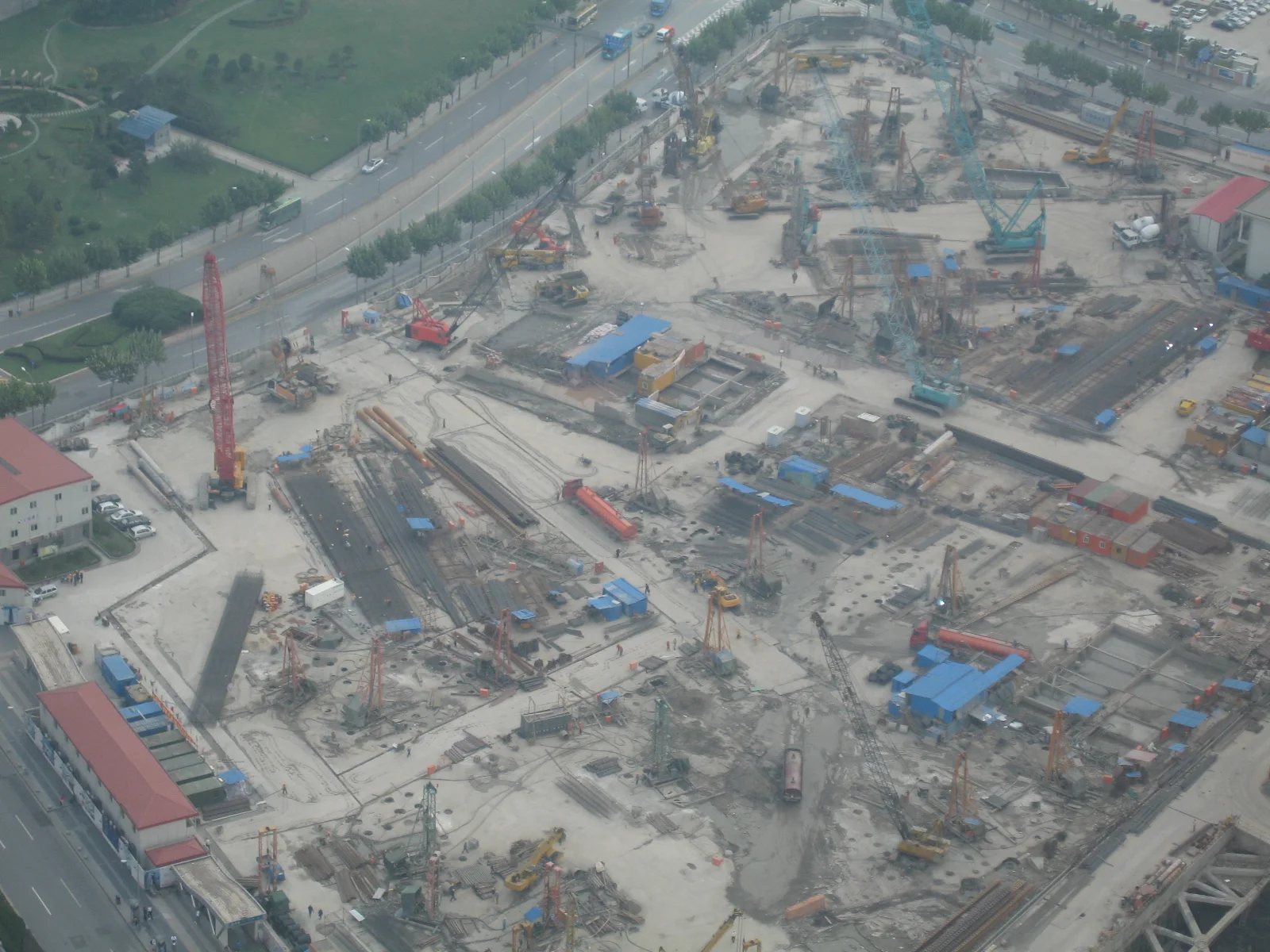 An overhead view looks down on a large building site with excavated ground, machinery, cranes and temporary structures.