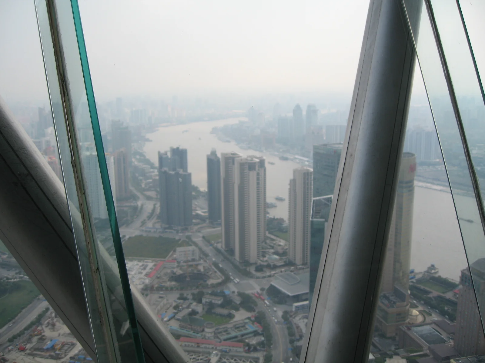 Sloping glass panels and large structural supports frame an elevated view of apartment blocks and streets.