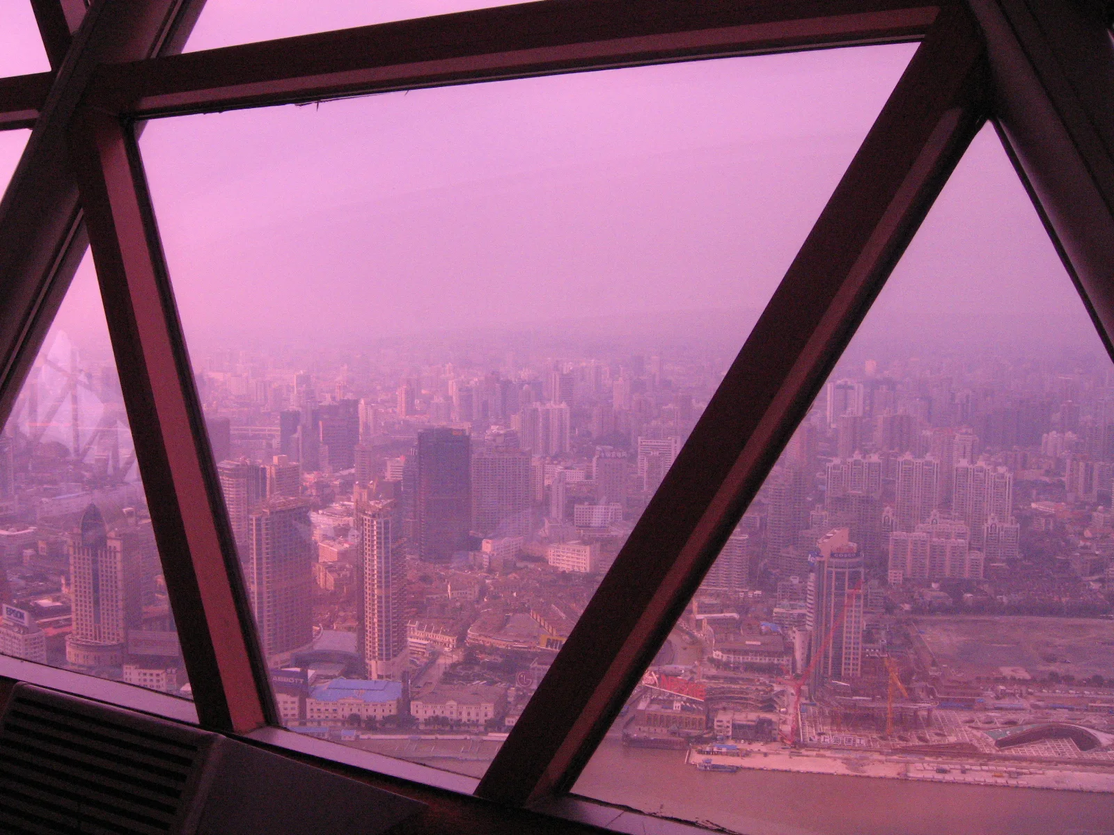 Angled window frames divide a city view tinted pink by coloured glazing.