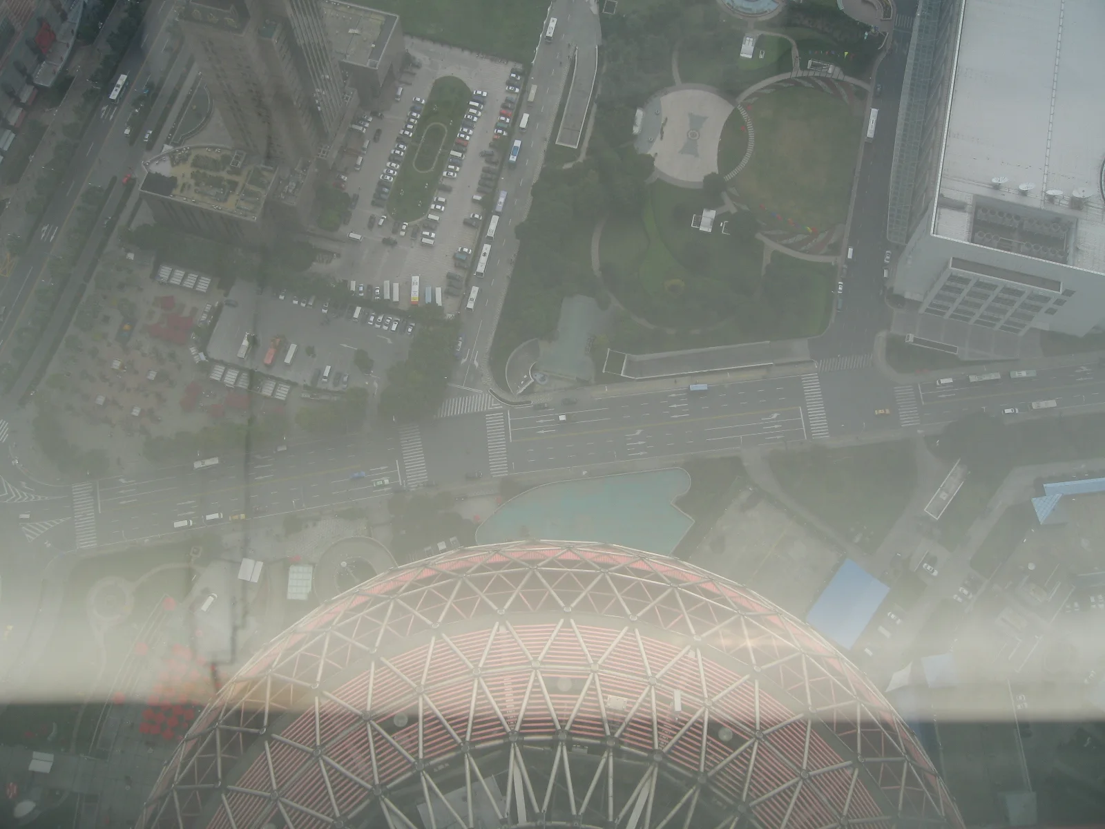 A steep downward view through glass takes in streets and the upper edge of a curved lattice-covered structure.