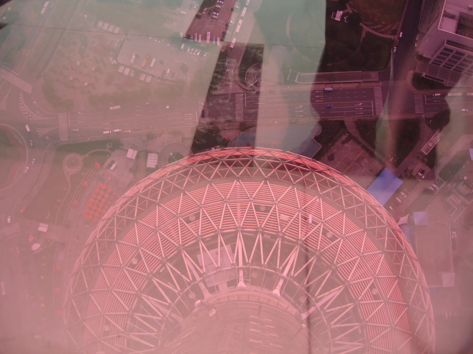 Reflections and pink-tinted glazing overlay a downward view of a rounded structure with a triangular framework.