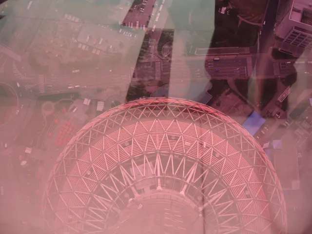 Reflections and pink-tinted glazing overlay a downward view of a rounded structure with a triangular framework.