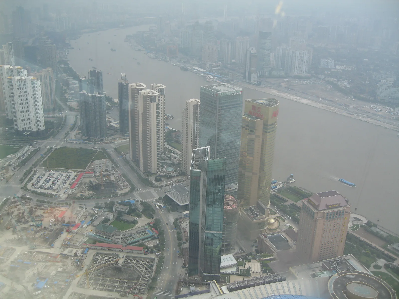 An elevated view looks over several towers, construction areas and the broad river fading into haze.
