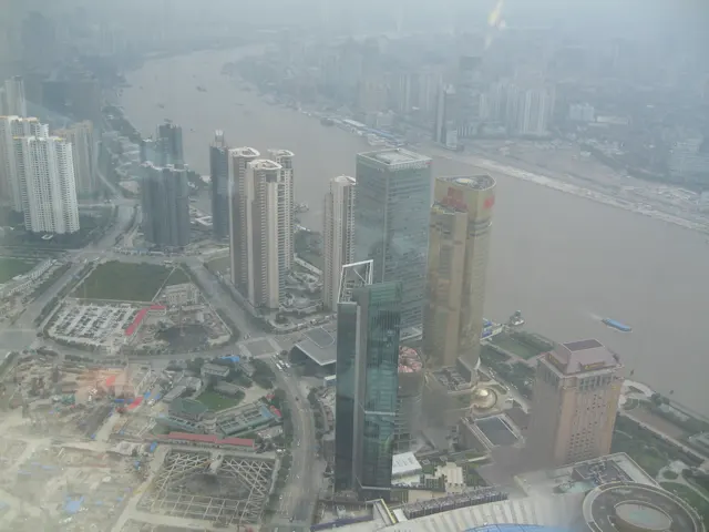 An elevated view looks over several towers, construction areas and the broad river fading into haze.
