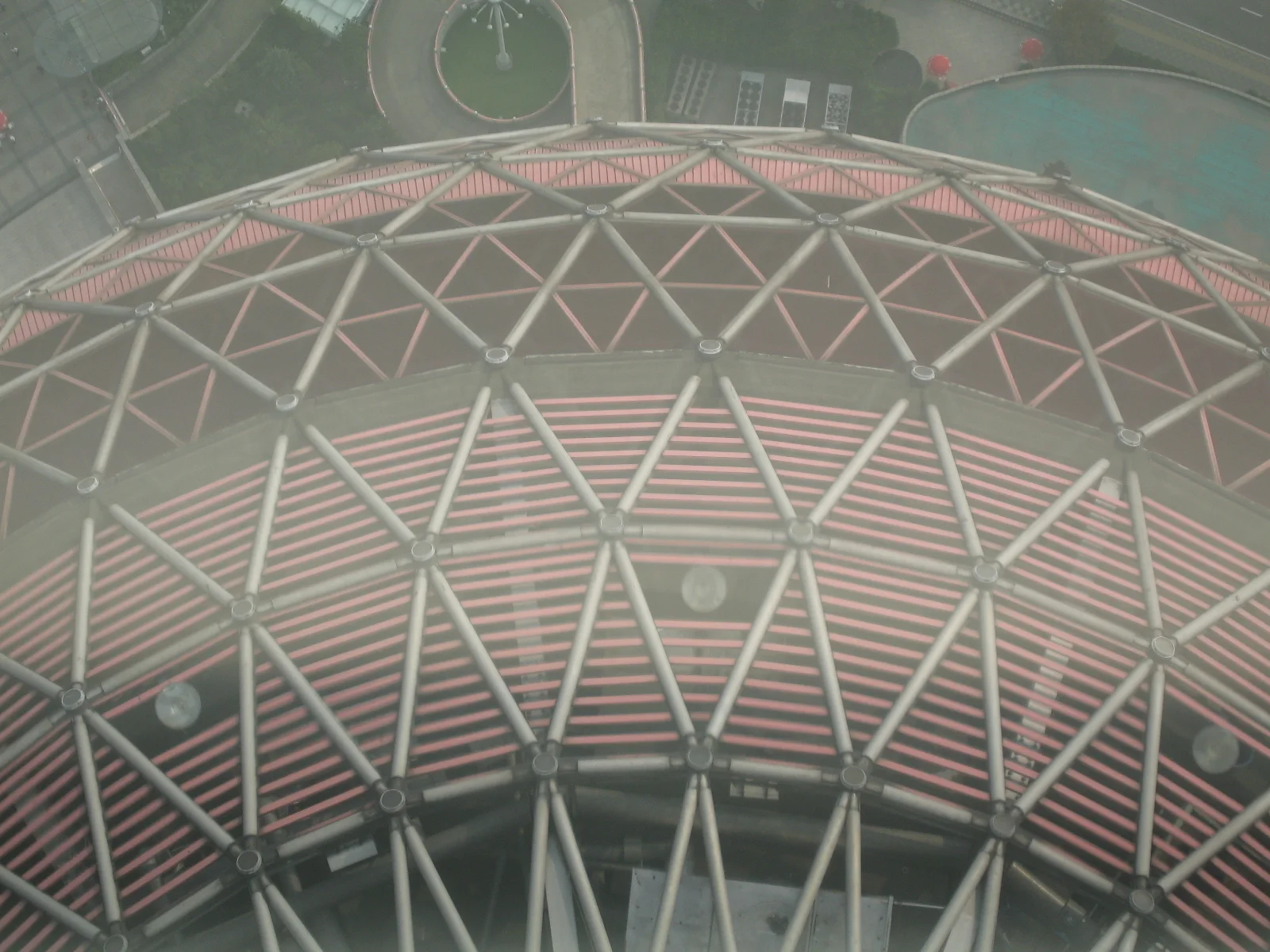A close downward view shows a rounded red-and-white structure covered by repeating triangular supports.