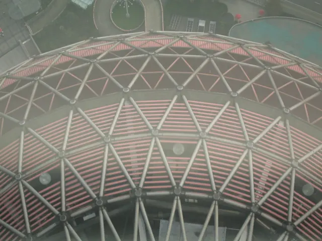 A close downward view shows a rounded red-and-white structure covered by repeating triangular supports.