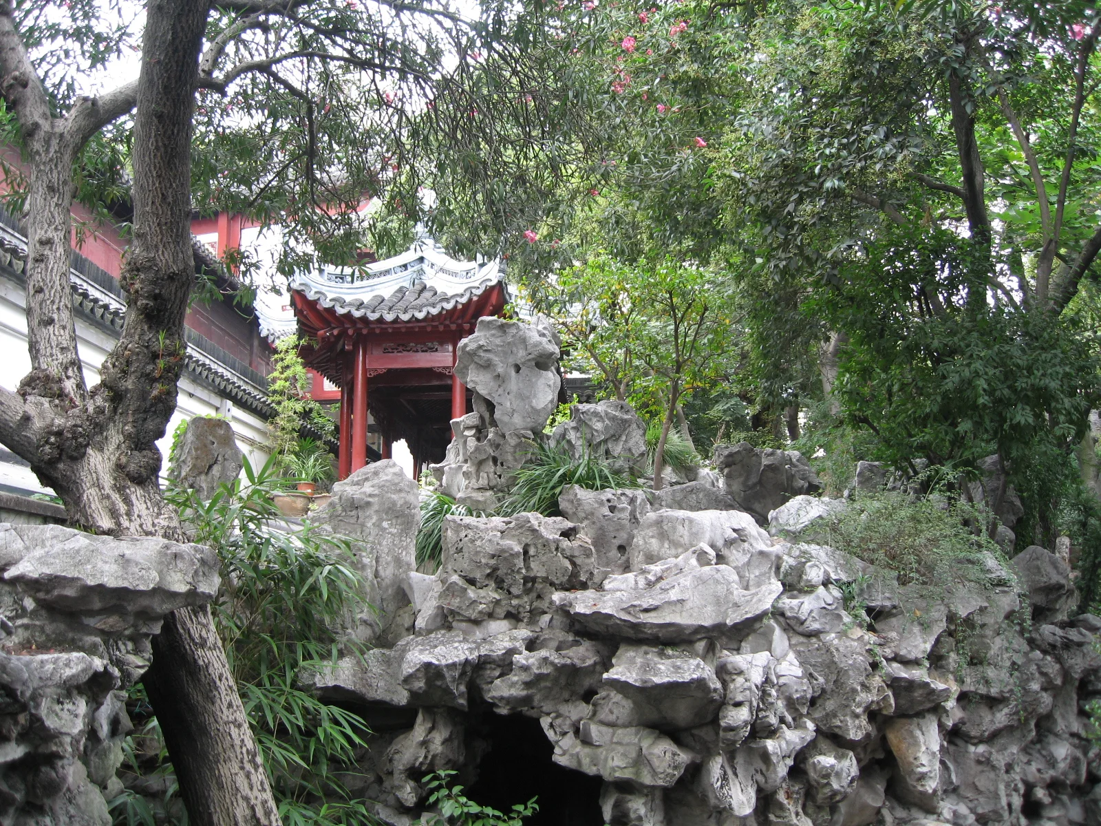 Layered grey rocks rise beneath leafy trees beside a red pavilion with a curved tiled roof.