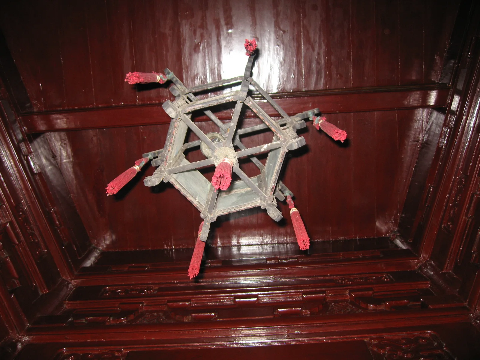 A geometric hanging fixture with pale spokes and red details sits beneath a glossy dark-red wooden ceiling.